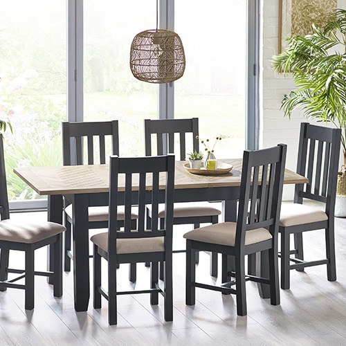 A wooden Bordeaux dining table with six chairs placed in a spacious dining room with ample natural light. The table is adorned with a white vase of flowers and dinnerware, while the chairs are upholstered in beige fabric. This image is part of an article titled "Does the dining room have to be next to the kitchen?
